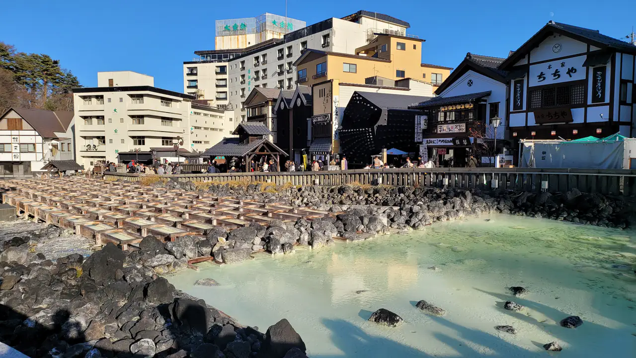 Hot spring water flowing along rows of wooden channels into a pale turquoise pool in the centre of an onsen town