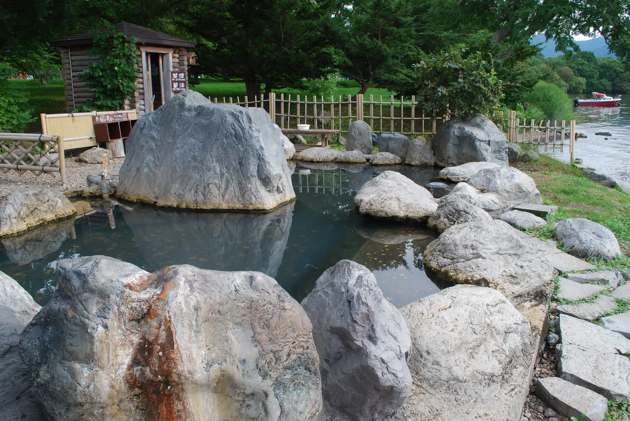 Huge smooth boulders forming a natural stone bath, with a small wooden hut and lake shore behind