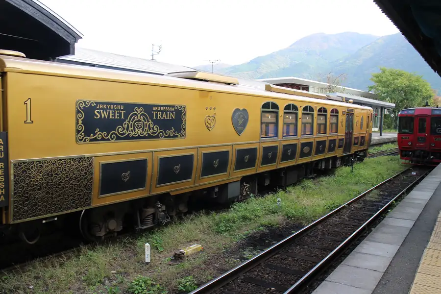The gold and black Aru Ressha with ornate gold trim and arched windows at a country station